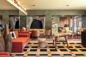 A modern hotel lobby with a checkered floor, red sofas, wooden chairs, and a coffee bar. - Kimpton Atlantico Algarve (Albufeira)