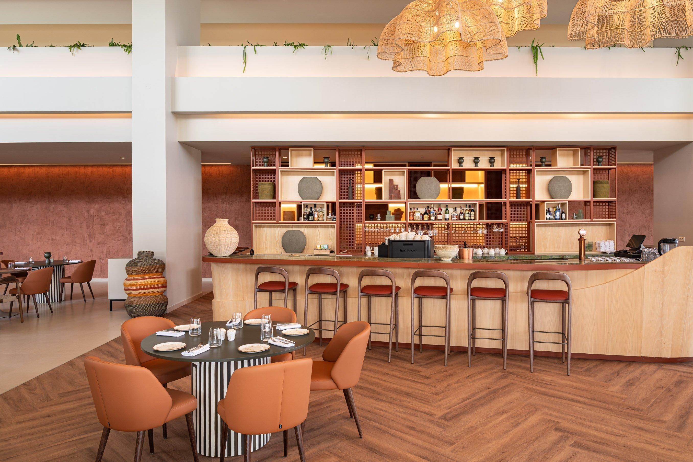 Een moderne barruimte met een ronde centrale tafel en meerdere barkrukken, omringd door planken met diverse flessen en decoratieve objecten.