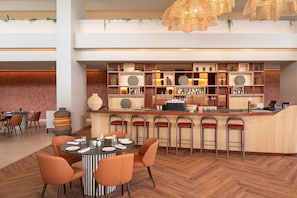 A modern bar area with a central round table and multiple stools, surrounded by shelves with various bottles and decorative items. - Kimpton Atlantico Algarve (Albufeira)