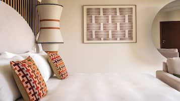 A hotel room with a bed, pillows, a wall-mounted lamp, and a framed artwork.