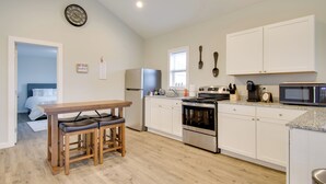 Eine moderne Küche mit weißen Schränken, einem Edelstahlkühlschrank, einem Backofen, einer Mikrowelle und einem Essbereich mit einem Holztisch und zwei Stühlen.