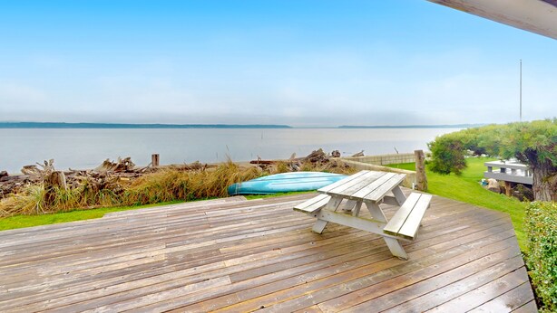 Eine Holzterrasse mit Picknicktisch mit Blick auf einen Strand und den Ozean.