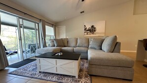 Ein modernes Wohnzimmer mit einer Eckcouch, einem Couchtisch und einem großen Fenster mit Vorhängen.