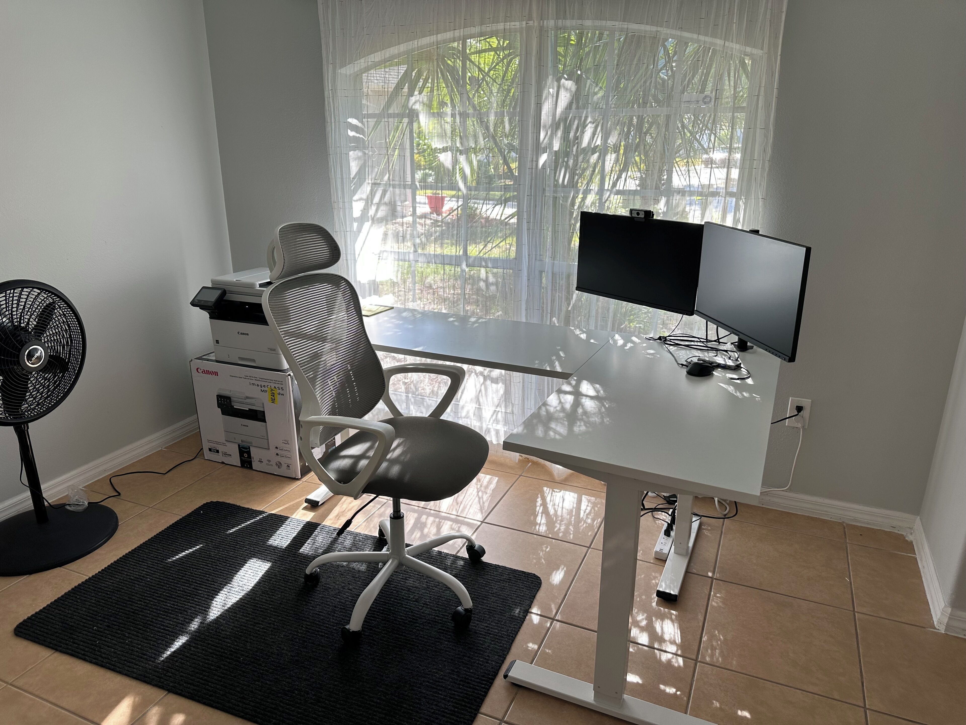 A modern office space with a white desk, a computer monitor, a printer, a fan, and a chair.