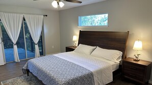 Ein Schlafzimmer mit einem Bett, zwei Nachttischen mit Lampen, einem Deckenventilator, einem Fenster mit Blick und einer Glastür zu einem Außenbereich.