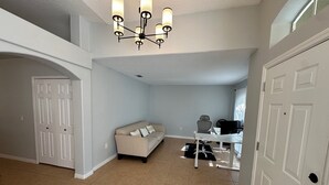 Ein geräumiges Wohnzimmer mit einem beigefarbenen Sofa, einem Essbereich mit Tisch und Stühlen, einem schwarzen Bürostuhl und einer Kristallleuchter.