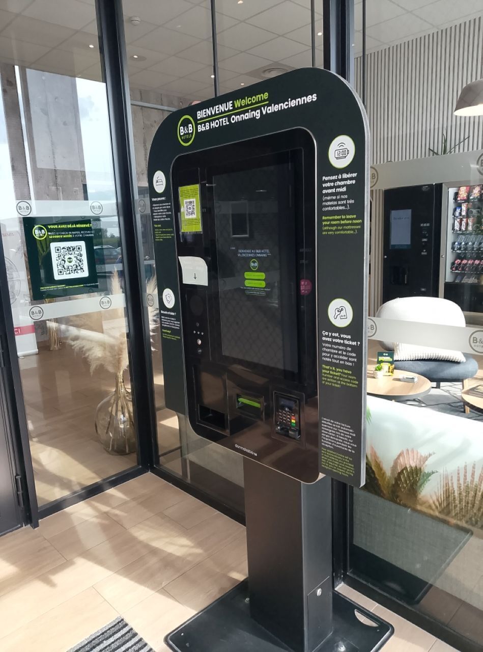 A self-service kiosk at the entrance of a hotel with a QR code and instructions for room selection.