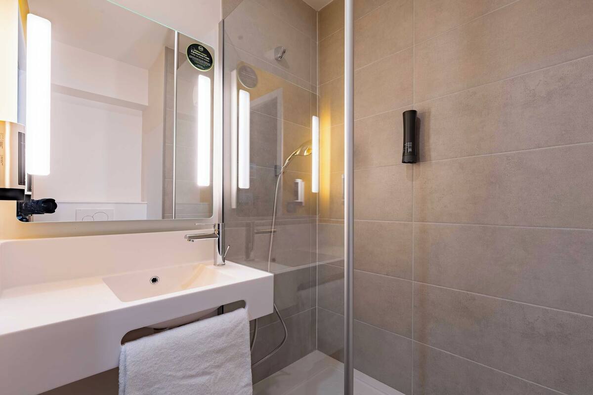 Een moderne badkamer met een witte wastafel, een douchecabine van glas en een handdoek aan de muur.