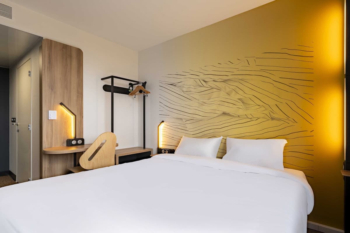 Een hotelkamer met een bed, nachtkastjes, een bureau en een kapstok aan de muur.