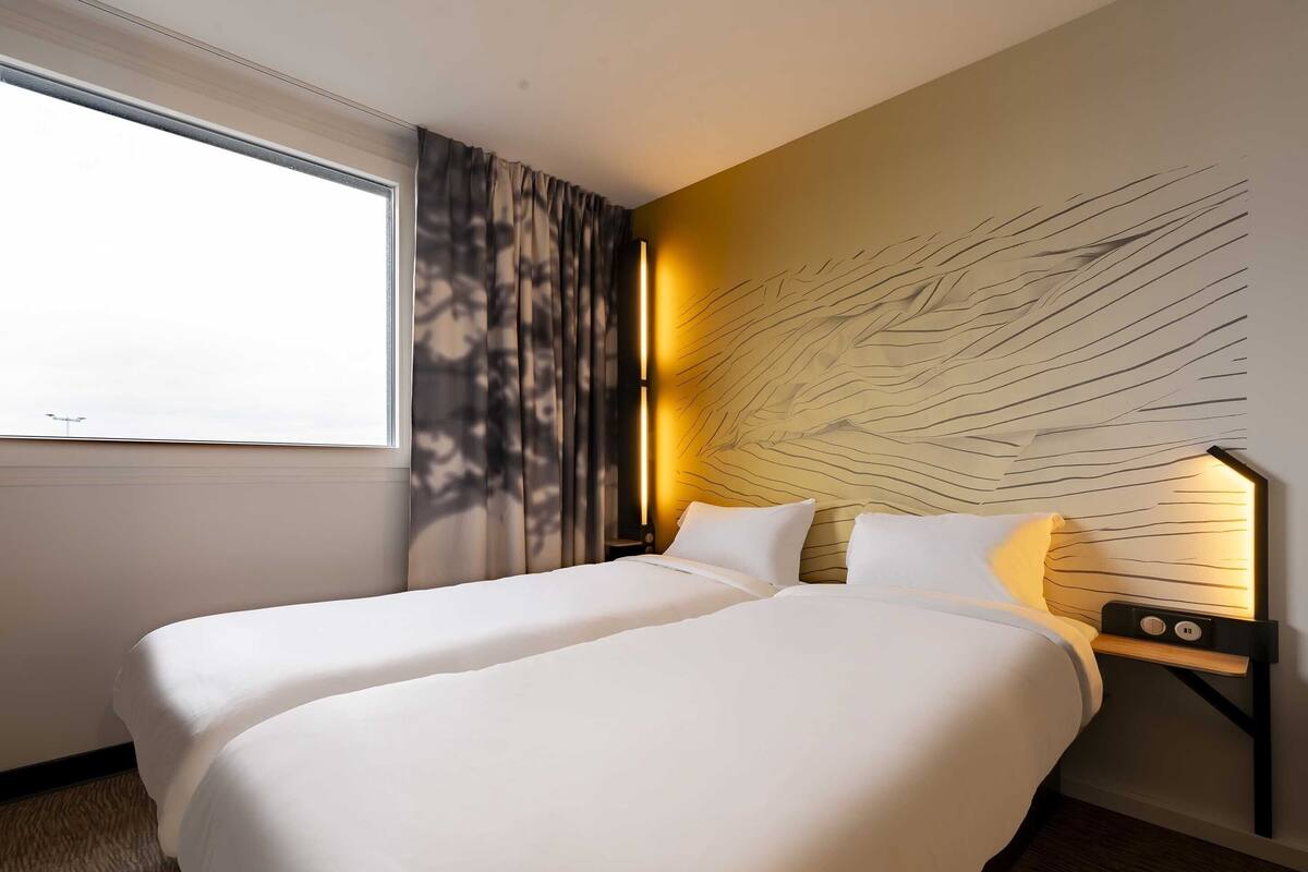 Een hotelkamer met een groot bed, een nachtkastje, een wandlamp en een raam met gordijnen.