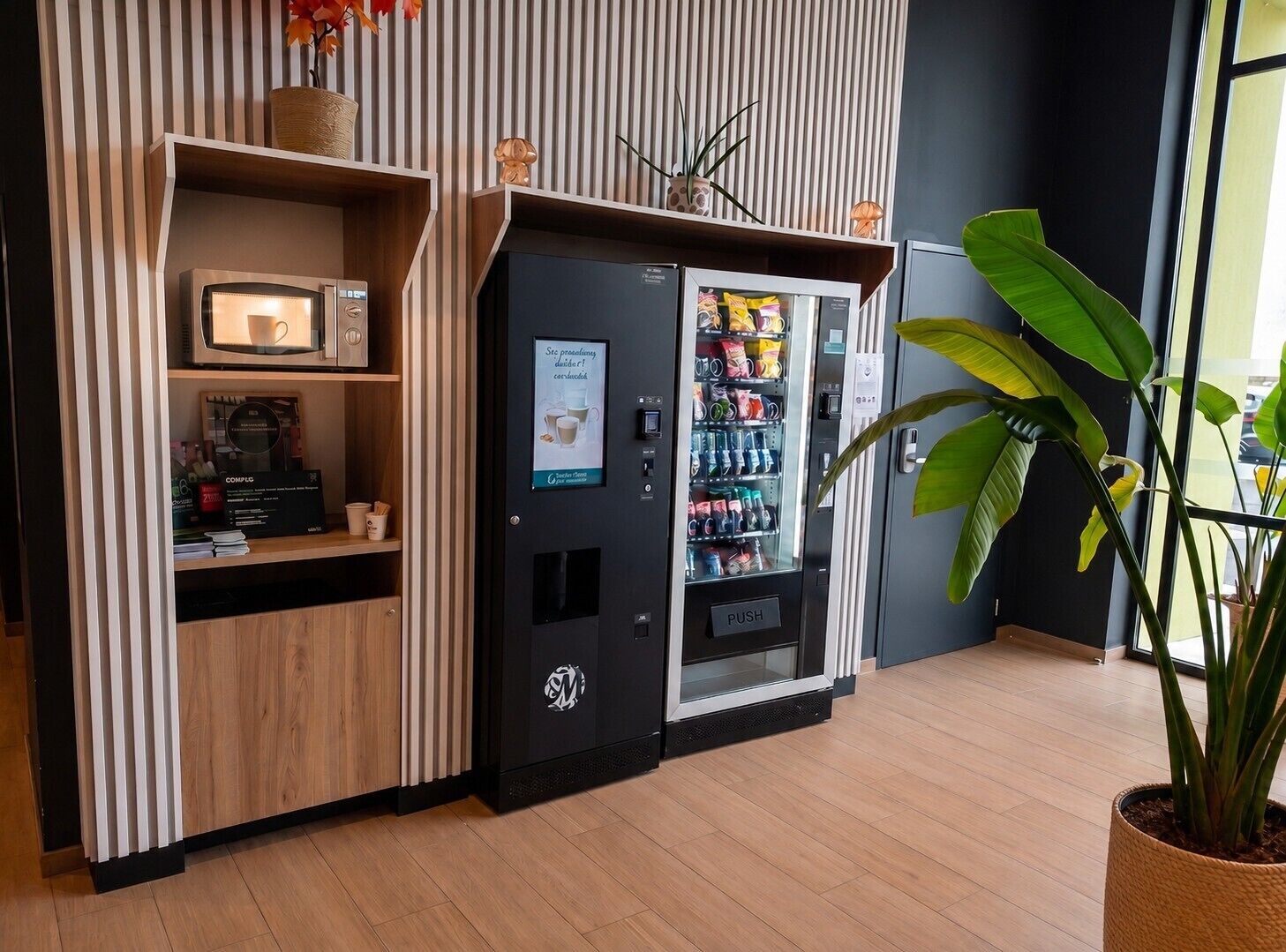 A vending machine with a push button, a coffee machine, and a shelf with books and a coffee cup.