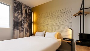 Ein Hotelzimmer mit einem Bett, einem Nachttisch, einer Wandlampe, einer Holzkommode und einem Spiegel.