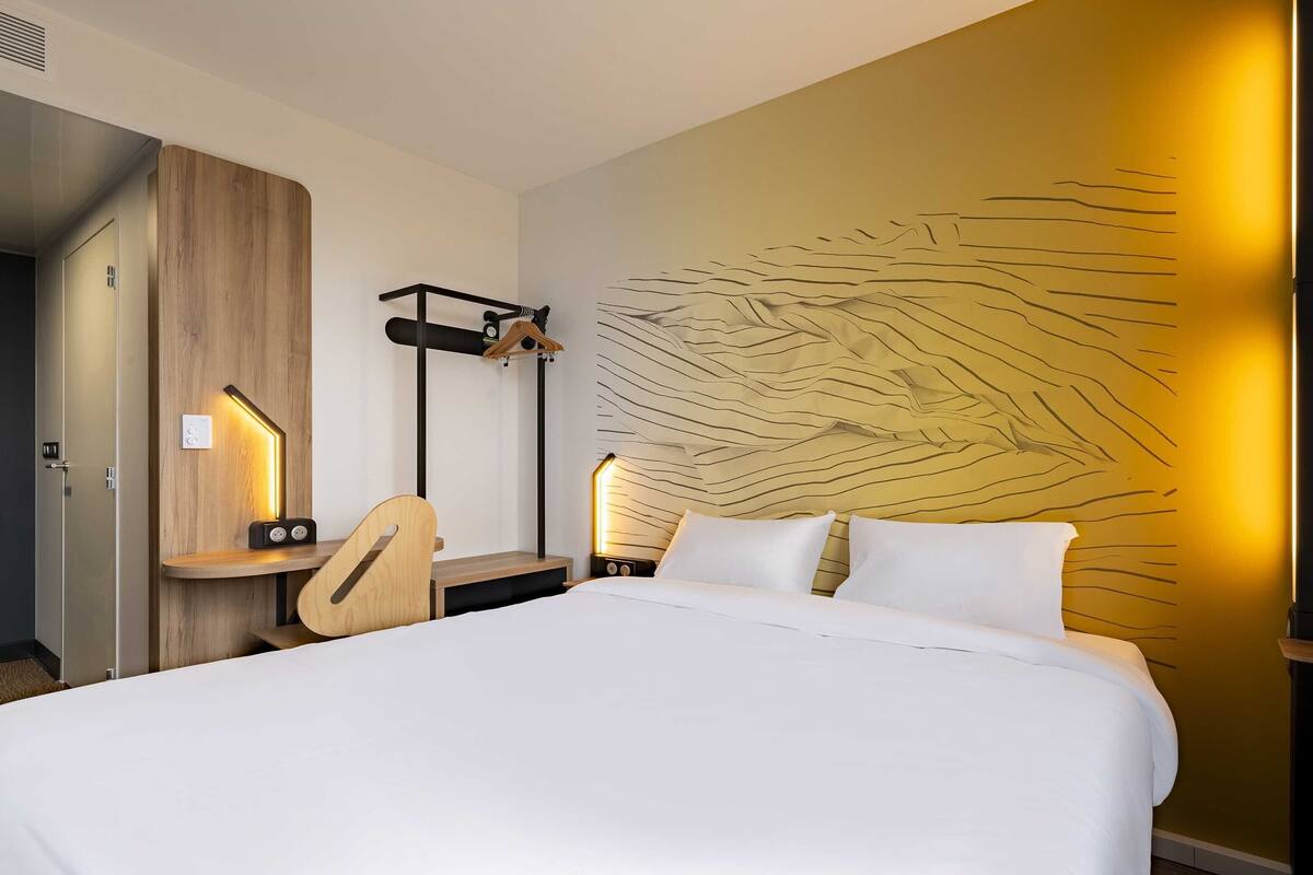 Een hotelkamer met een bed, nachtkastjes, een bureau en een kapstok aan de muur.