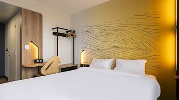 Una habitación de hotel con cama, mesitas de noche, escritorio y perchero en la pared.