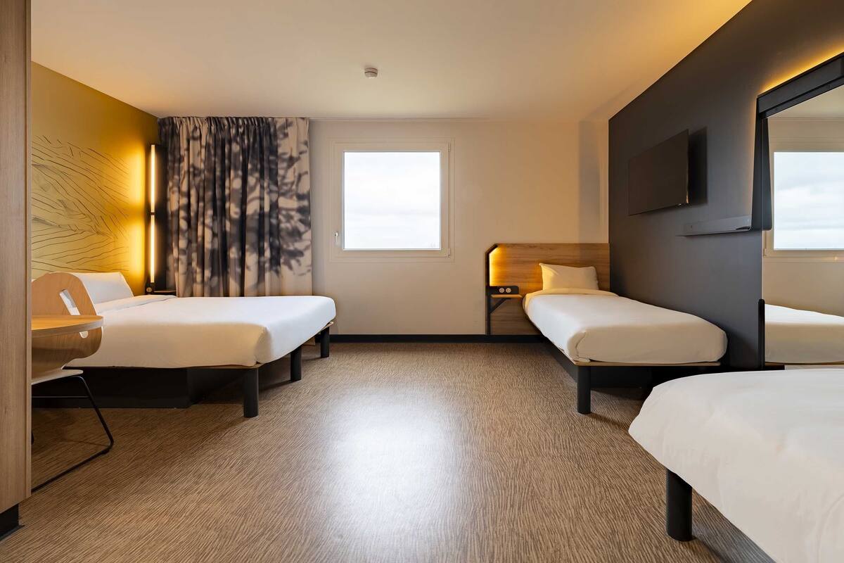 Een hotelkamer met twee bedden, een bureau, een stoel, een televisie en een raam.