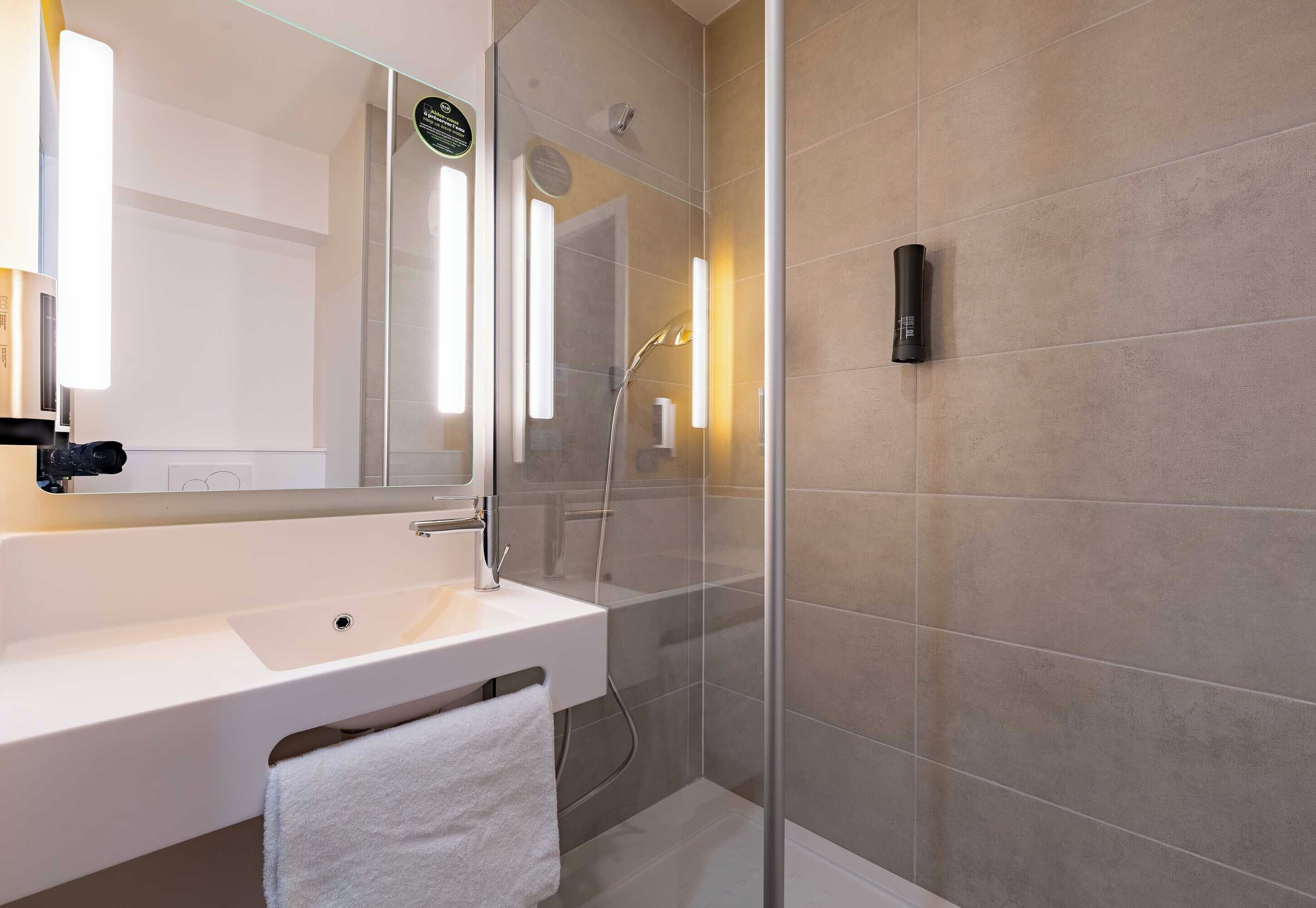 Een moderne badkamer met een witte wastafel, een douchecabine van glas en een handdoek aan de muur.