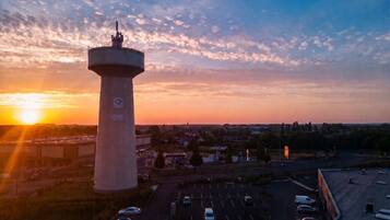 Una torre cilíndrica grande con la parte superior plana, rodeada por un estacionamiento con varios autos, con el cielo al atardecer como fondo.