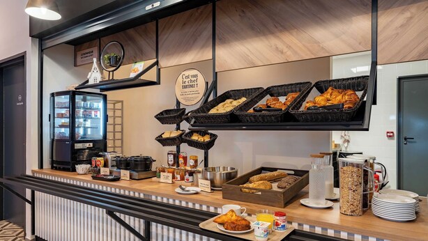 Ein Frühstücksbuffet mit verschiedenen Speisen, einem Kühlschrank und einem Schild, das die Frühstückszeiten angibt.