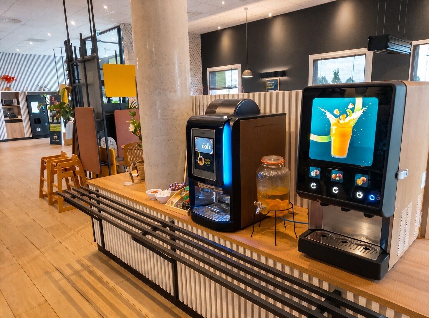 A modern coffee station with a coffee machine, a juice dispenser, and a glass jar of orange juice.