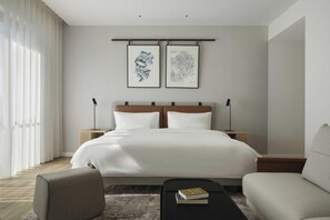 Una habitación de hotel moderna con una cama grande, dos mesitas de noche, un sofá y una mesa de centro.