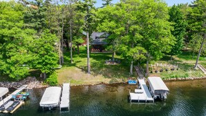 A lakeside property with docked boats, a cabin, and a fire pit area surrounded by trees. - Dock, Firepit & Cuyuna Trails at Serpent Lake (Crosby)