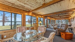 A cozy cabin interior with large windows, a glass dining table, and comfortable seating. - Dock, Firepit & Cuyuna Trails at Serpent Lake (Crosby)