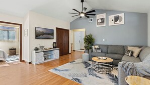 Ein modernes Wohnzimmer mit grauem Sofa, einem Couchtisch und einem an der Wand montierten Fernseher.