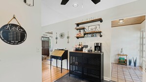 A kitchen area with a black countertop, wooden shelves, and a coffee machine. There is a sign on the wall and a small table with a plant. - Doras Dream, 4 Bedrooms, Sleeps 12, Downtown (Mount Dora)