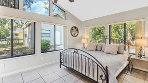 A bedroom with a large bed, two bedside tables, a ceiling fan, and large windows offering views of the outdoors. - Doras Dream, 4 Bedrooms, Sleeps 12, Downtown (Mount Dora)