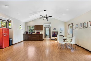 A spacious kitchen with wooden flooring, a ceiling fan, and a dining area with white chairs and a glass table.