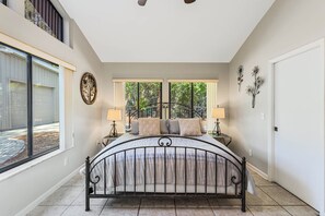 A bedroom with a large bed, two bedside lamps, a window with a view of trees, and a decorative wall piece.