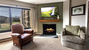 A living room with a fireplace, a television mounted above it, and two armchairs.