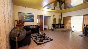 A spacious living room with a black sofa, a standing fan, a wooden coffee table, and a large painting on the wall. - Idiroko estate - Green, Beautiful, Quiet and Central (Lagos)