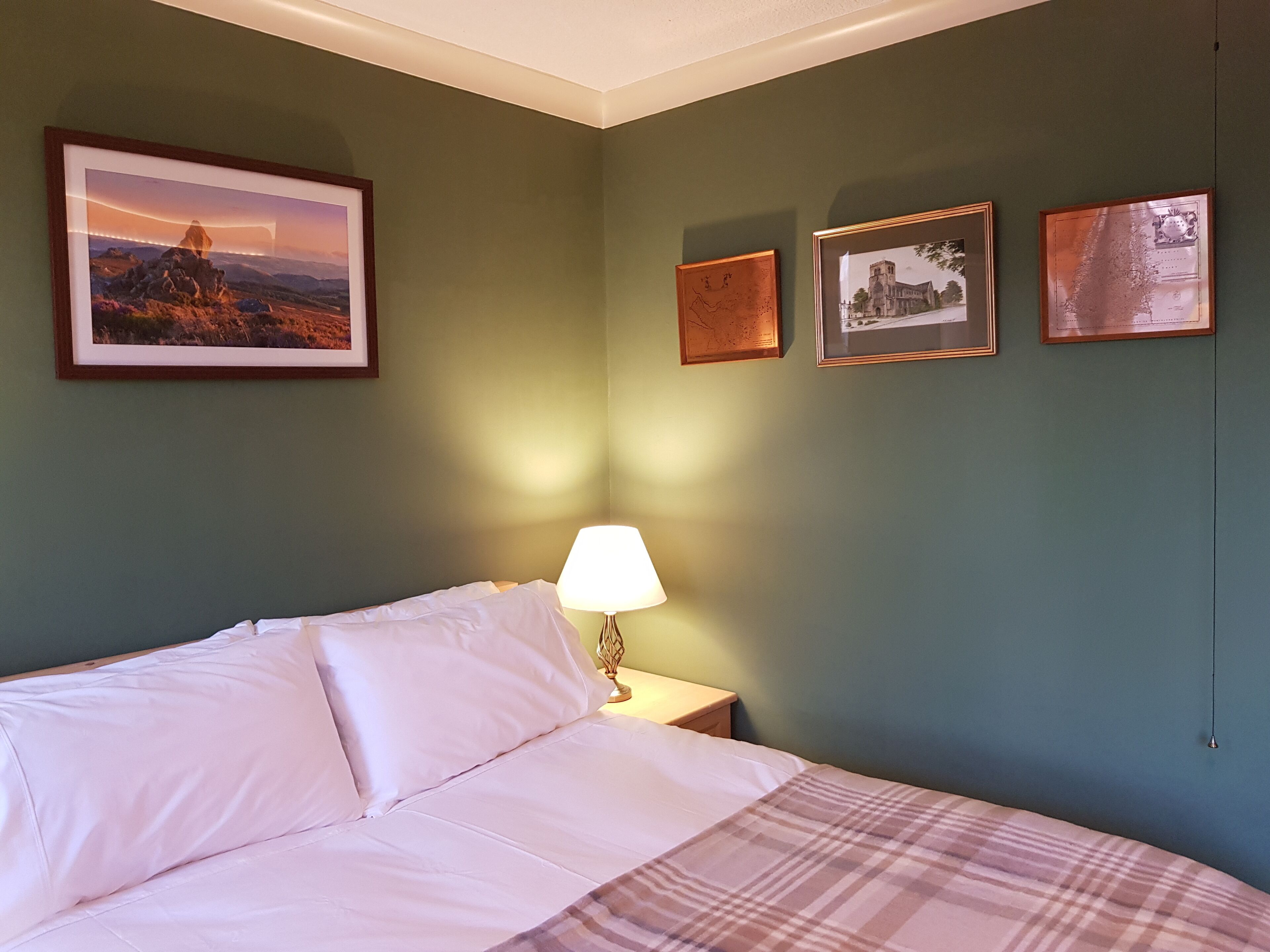 A bedroom with a bed, a nightstand, a lamp, and three framed pictures on the wall.