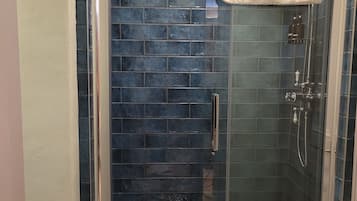 Een glazen douchecabine met een betegelde wand, een witte handdoek hangend aan de deur en een douchekop.