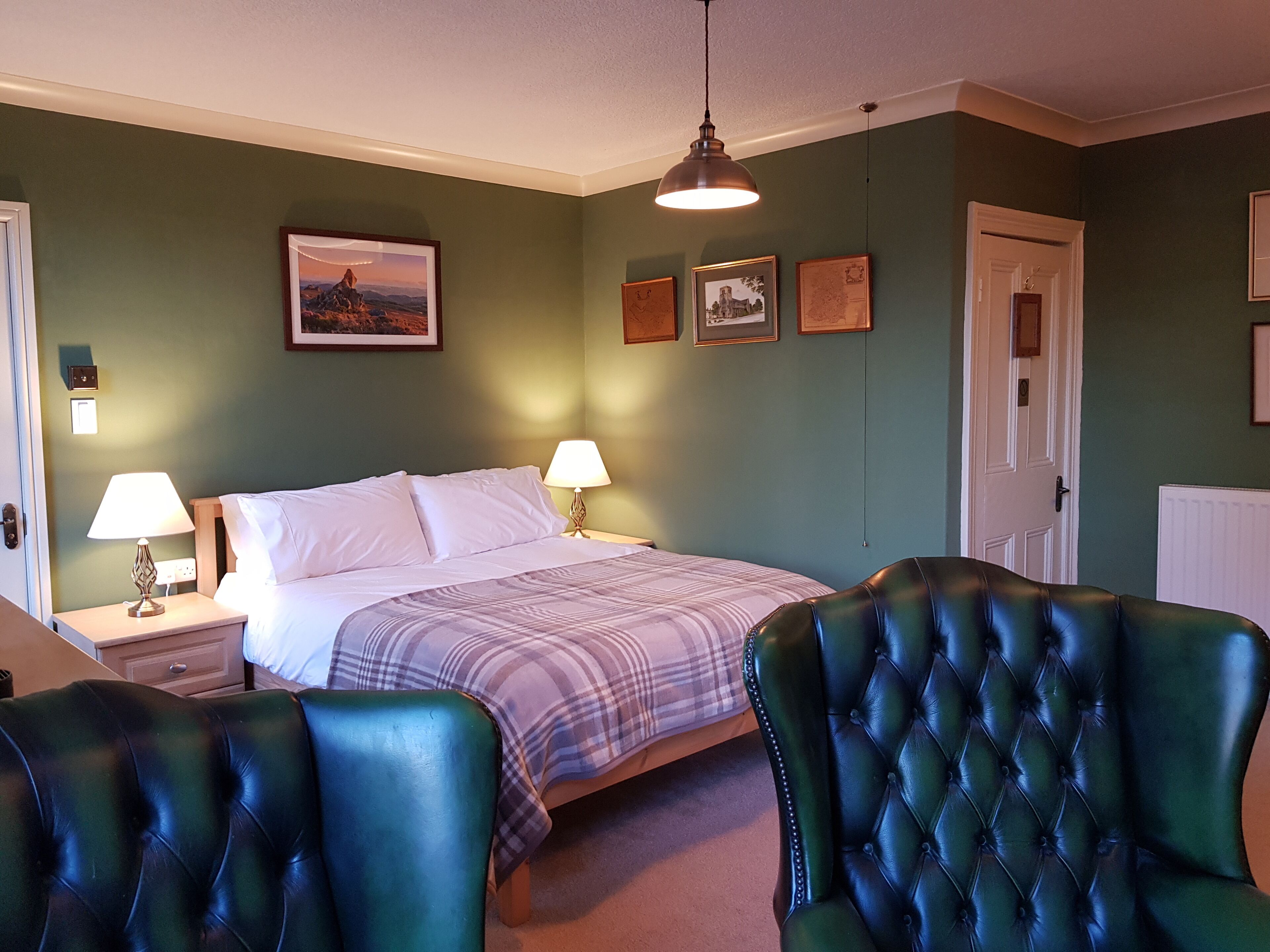 Een slaapkamer met een bed, twee nachtkastjes met lampen, een deur en een wand met ingelijste foto’s.