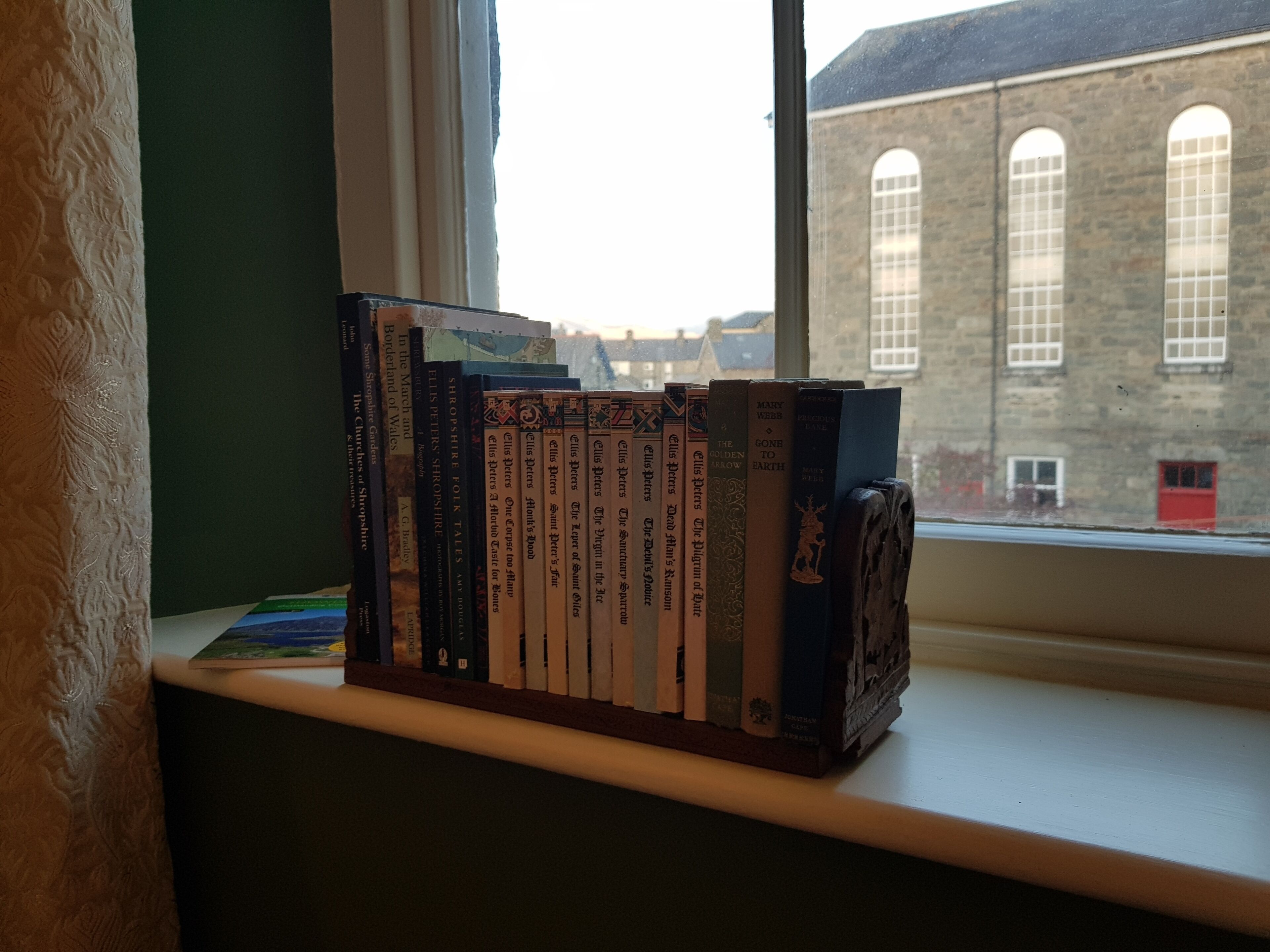 Una estantería con libros sobre un alféizar, con vista a un edificio con ventanales de arco.