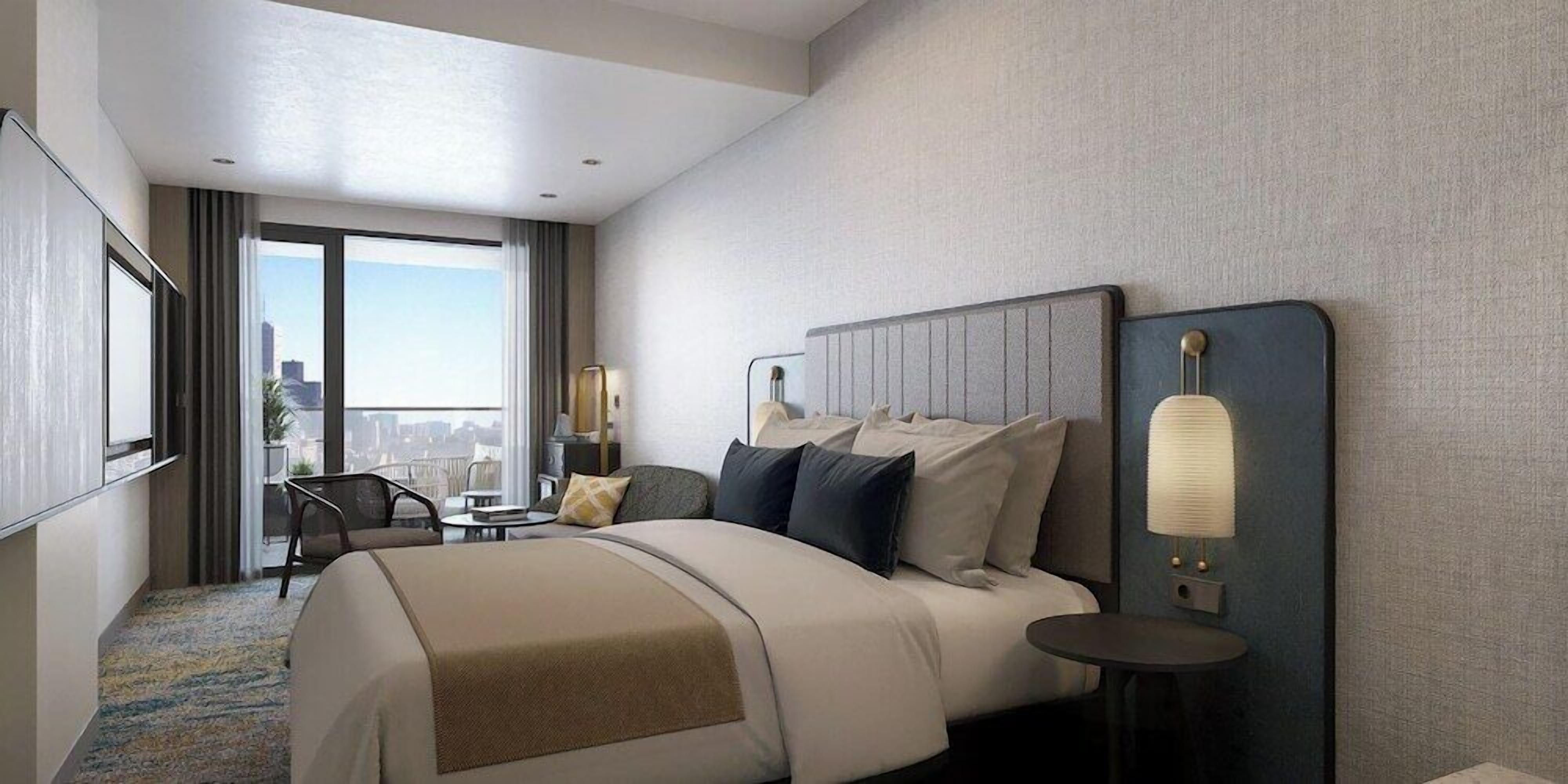 A hotel room with a large bed, a desk, a chair, a lamp, and a view of the city.