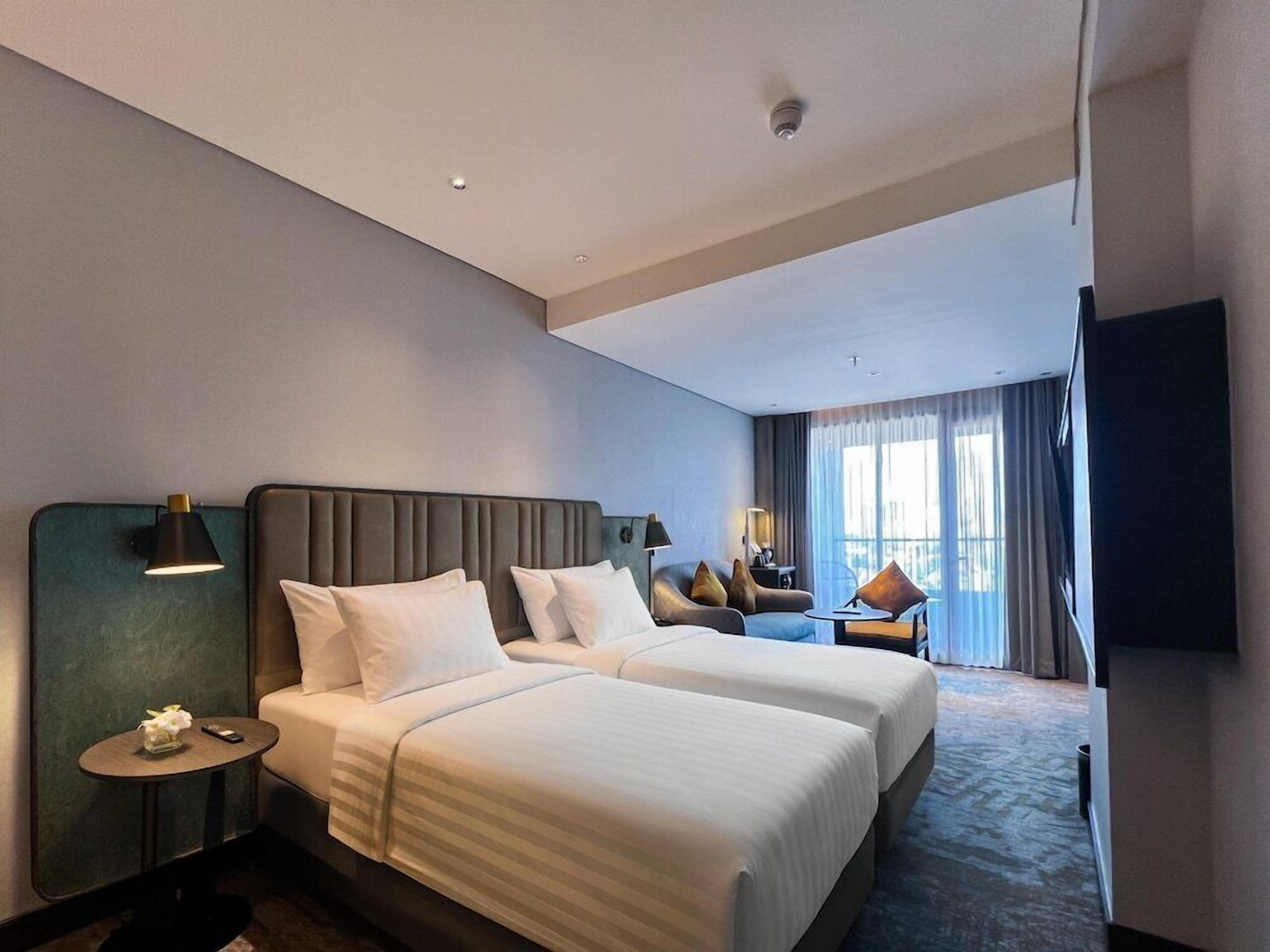 A hotel room with two beds, a small table, a chair, a TV, and a large window.