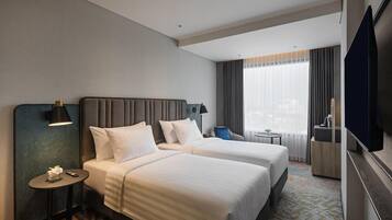 A hotel room with two beds, a TV, a small table, and a window with curtains.