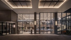 The exterior of the Mercure Hotel with a modern design, large glass entrance, and a visible staircase. - Mercure Madiun (Madiun)