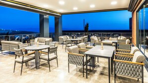 Un área de estar al aire libre con mesas y sillas, vistas a la ciudad y un diseño arquitectónico moderno.