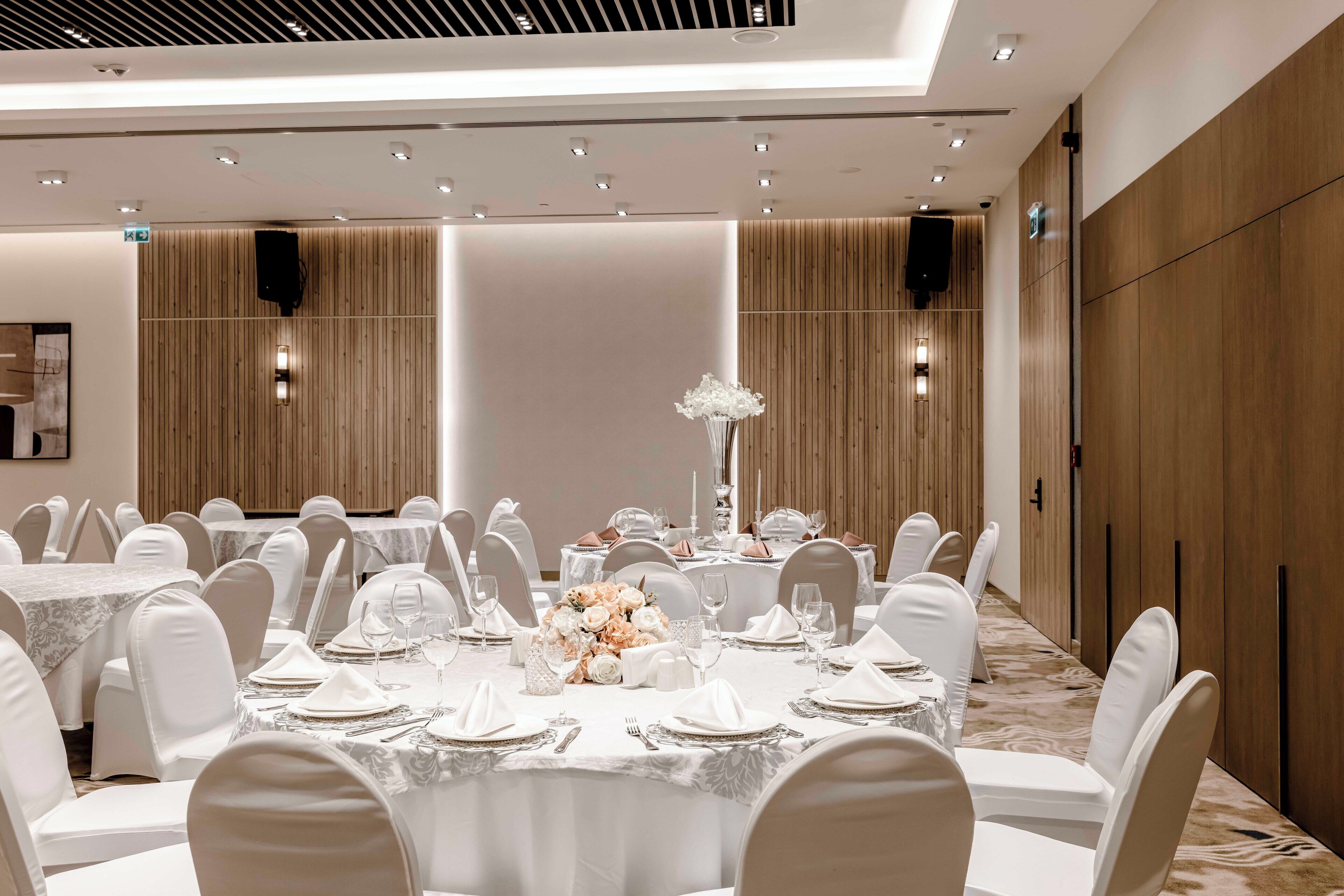 A banquet hall with round tables set for dining, white chairs, and a central floral arrangement.