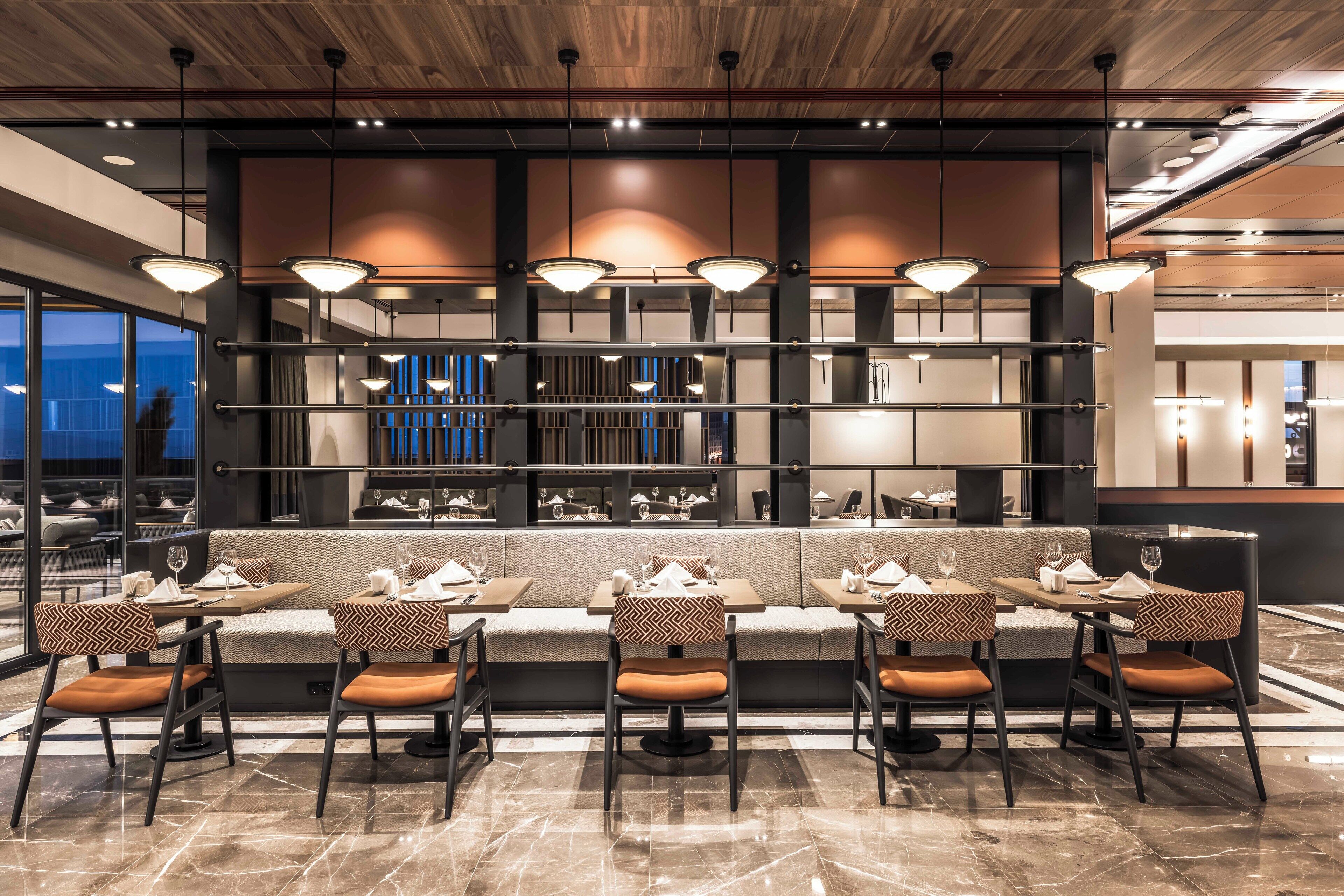 Un restaurante moderno con una barra alargada, asientos acolchados e iluminación colgante.