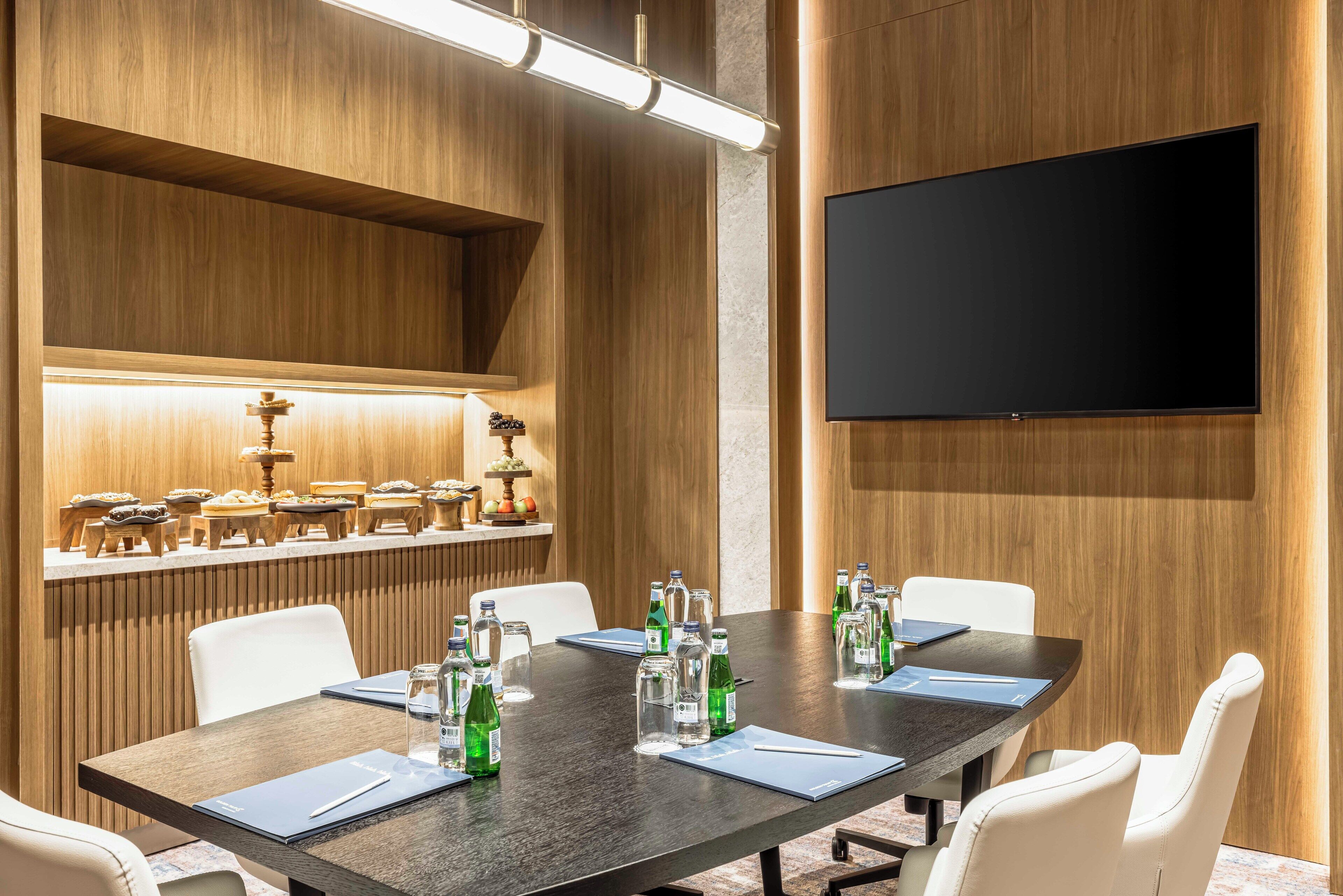 A conference room with a long table, white chairs, and a flat-screen TV mounted on the wall.