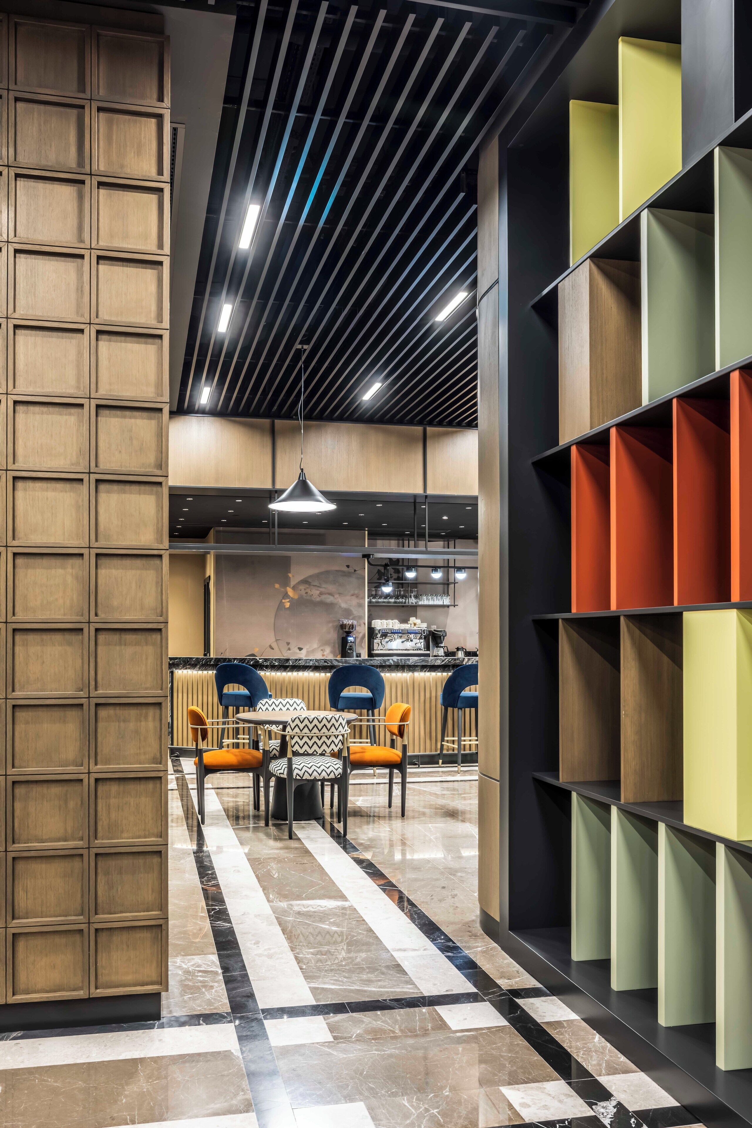 Un interior moderno con una zona de comedor central, una barra y un espacio de estar con estanterías de colores.