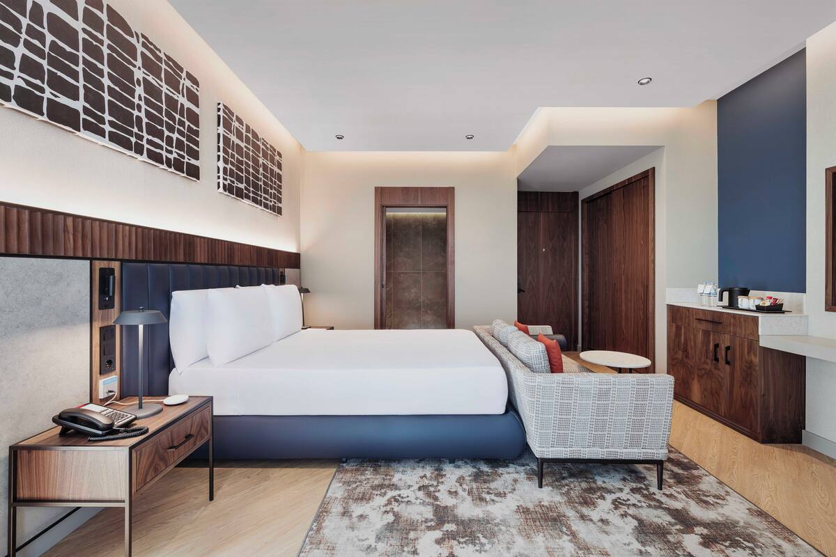Un dormitorio moderno con una cama grande, una mesita de noche, una lámpara y una pequeña mesa redonda con una silla.