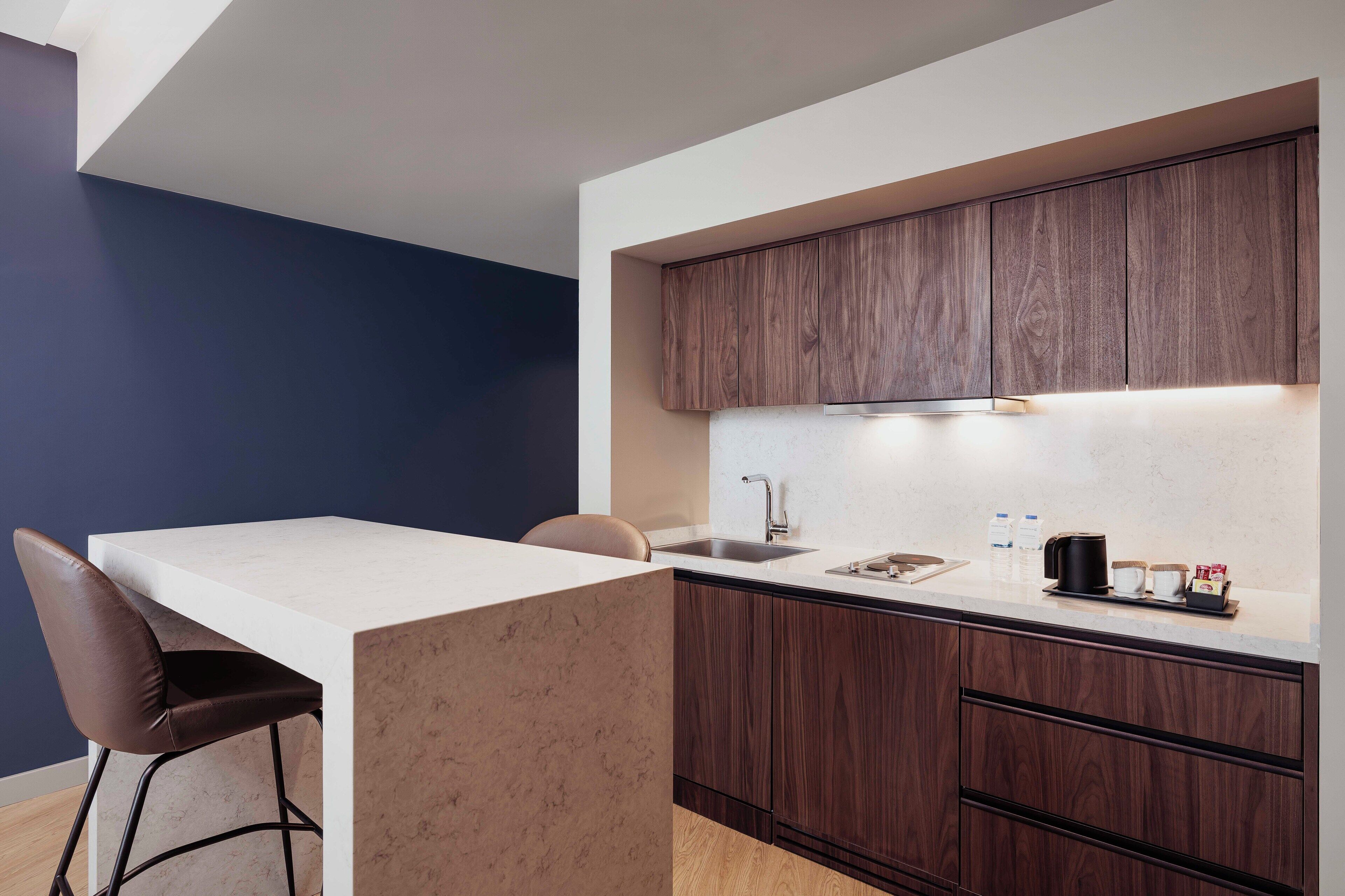 A modern kitchen with a white countertop, dark wooden cabinets, a built-in sink, and a bar stool.