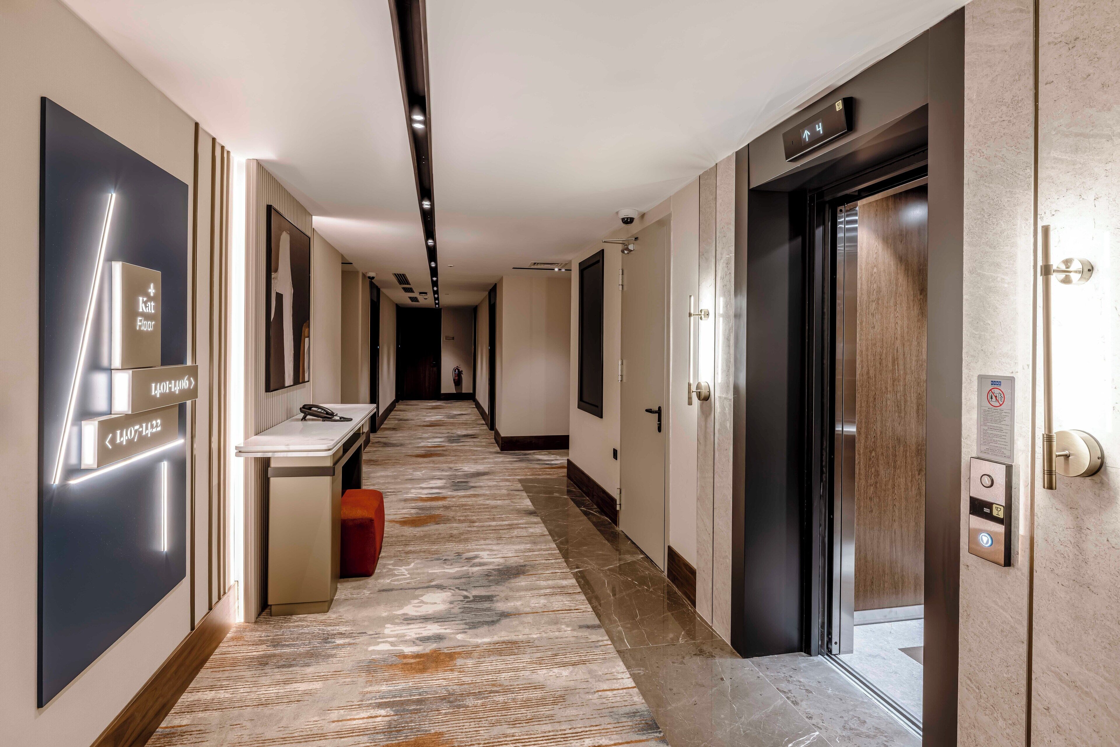 Un pasillo moderno de hotel con piso de mármol, una recepción y un ascensor.