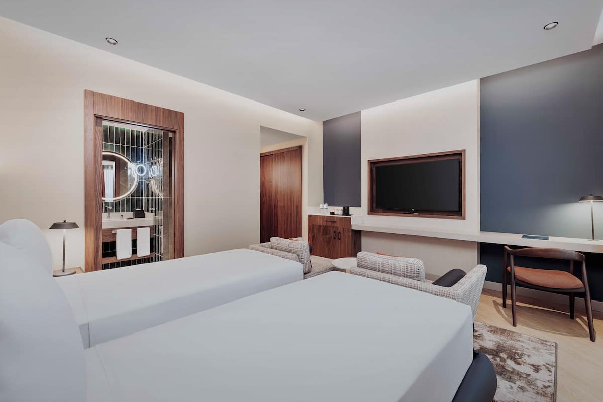 Una habitación de hotel moderna con una cama grande, un televisor montado en la pared, un escritorio y una zona de estar con una silla y sofá.
